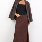 Woman wearing a brown coat, black top, and patterned skirt on a white background