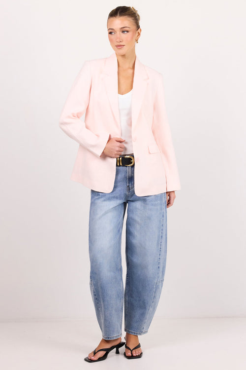 A woman modeling a light pink blazer, light-wash wide-leg blue jeans, a white top, and black sandals against a plain white studio background.