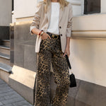 Woman in stylish outfit with leopard print pants and sunglasses standing against a building.