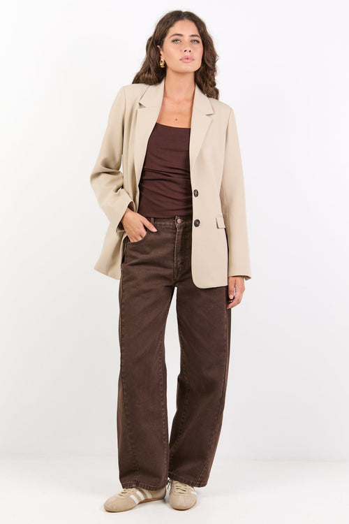 Woman wearing a beige blazer, brown top, and pants on a white background