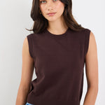 Woman wearing a brown sleeveless sweater and blue jeans against a white background