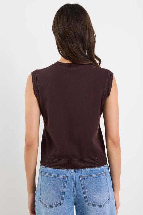 Person wearing a brown sleeveless top and blue jeans on a white background