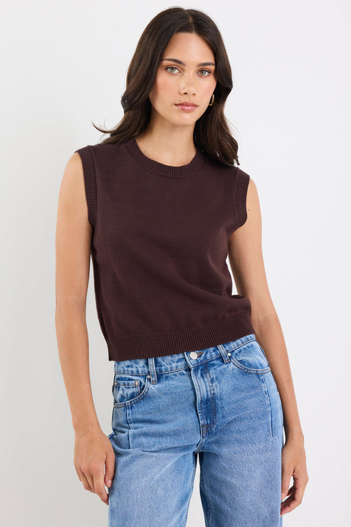 Woman wearing a brown sleeveless top and blue jeans against a white background