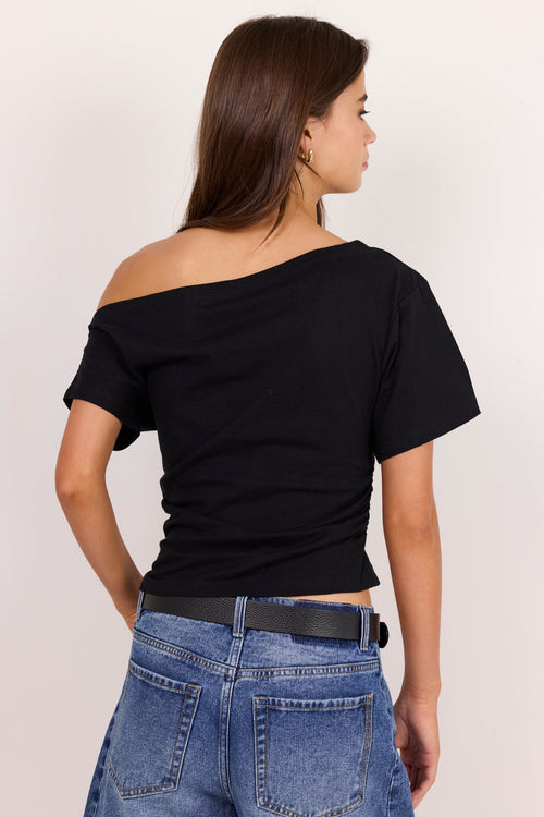 A woman shown from the back wearing a black off-the-shoulder short-sleeve crop top and blue jeans against a plain light background.