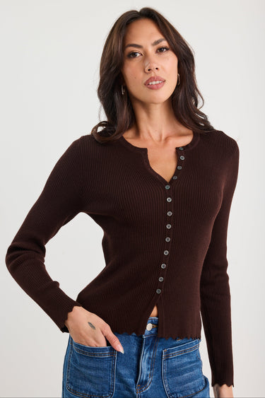 Woman wearing a brown ribbed long-sleeve top with buttons on a white background