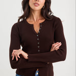 Woman wearing a brown ribbed sweater with buttons and blue jeans on a white background