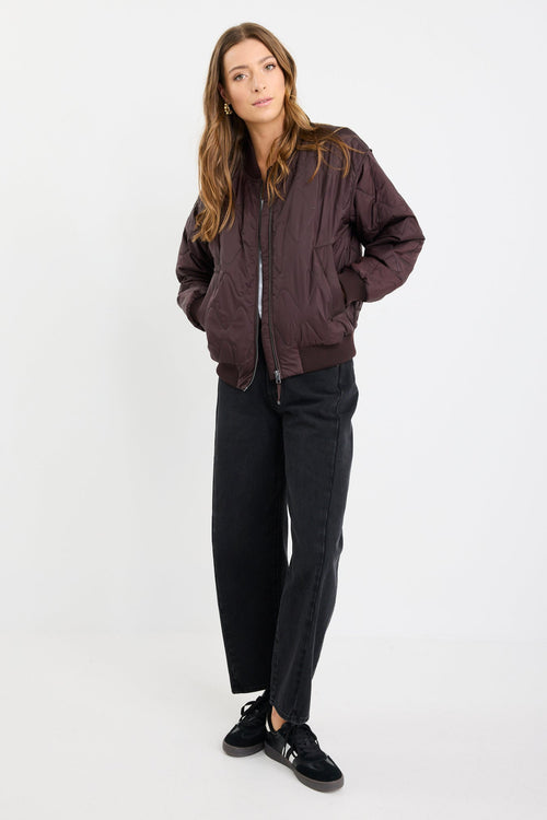 Woman wearing a brown bomber jacket and black pants on a white background