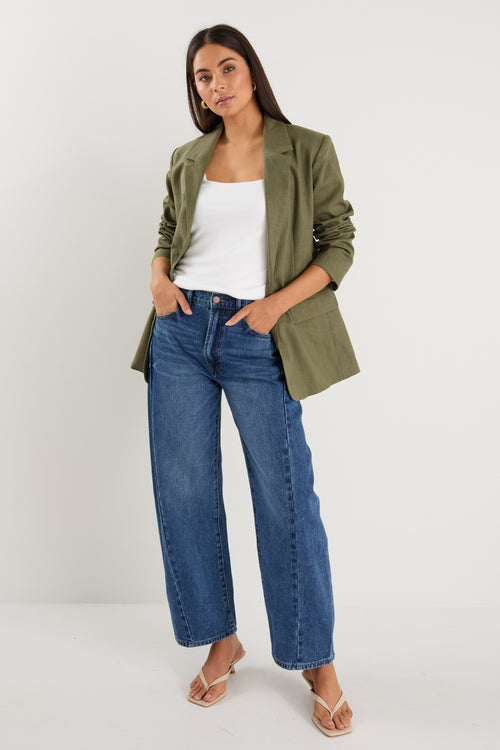 Model wears a green linen blazer with blue jeans