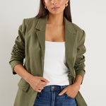 Model wears a green linen blazer with blue jeans