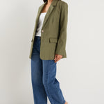 Model wears a green linen blazer with blue jeans