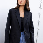 Woman wearing a black blazer and blue jeans against a white background