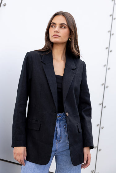 Woman wearing a black blazer and blue jeans against a white background