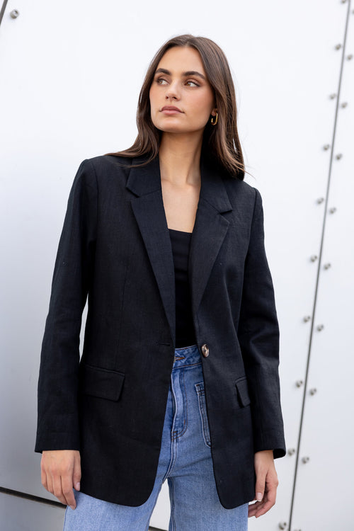 Woman wearing a black blazer and blue jeans against a white background