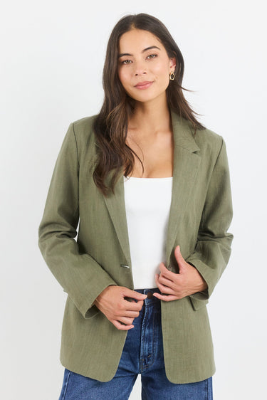Woman wearing an olive green blazer over a white top and blue jeans on a white background