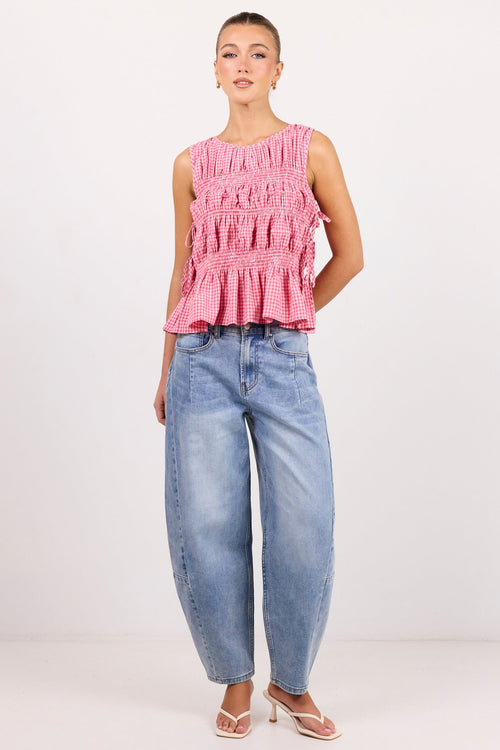 A woman modeling a sleeveless pink ruffled top and wide-leg light blue jeans against a plain white studio background.
