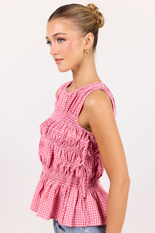 A woman wearing a pink and white gingham smocked sleeveless top, shown from a side profile against a plain white background.