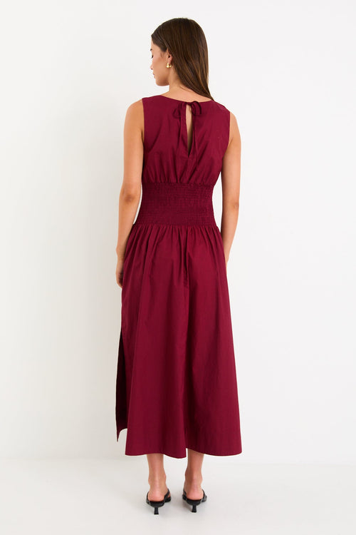 Model wearing a burgundy sleeveless maxi dress with a shirred waist and a flowing skirt.