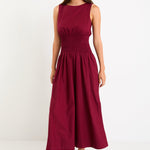 Model wearing a burgundy sleeveless maxi dress with a shirred waist and a flowing skirt.