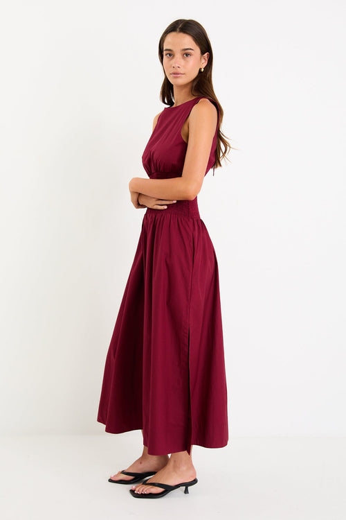 Model wearing a burgundy sleeveless maxi dress with a shirred waist and a flowing skirt.