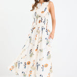 Woman wearing a sleeveless earthy botanical floral maxi dress with a shirred waist, tie detail, and a flattering, flowy silhouette.