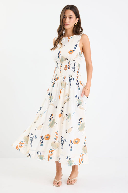 Woman wearing a sleeveless earthy botanical floral maxi dress with a shirred waist, tie detail, and a flattering, flowy silhouette.