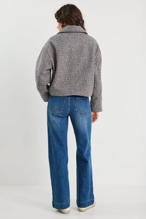 Person wearing a gray jacket and blue jeans on a white background