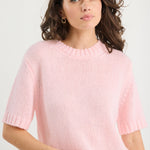 Woman wearing a pink sweater and blue jeans against a white background