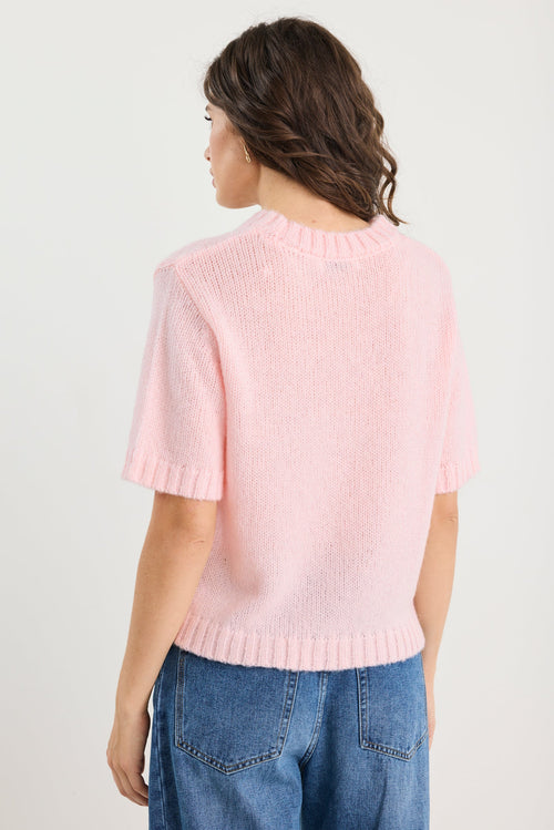 Person wearing a pink sweater and blue jeans on a plain background
