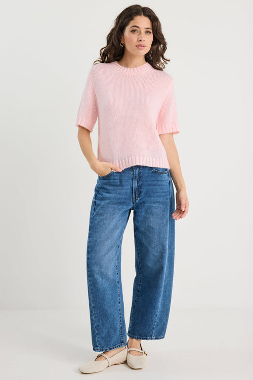 Woman wearing a pink sweater and blue jeans on a white background