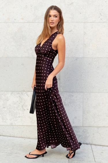 Woman in a dark dress with white polka dots standing against a light stone wall.