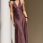 A woman wearing a sleeveless, floor-length mauve satin slip dress and sunglasses stands on stone steps beside white columns.