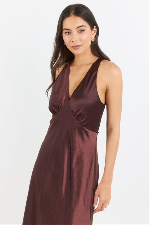 A woman modeling a sleeveless, deep V-neck midi dress in a rich burgundy satin fabric against a plain white studio background.