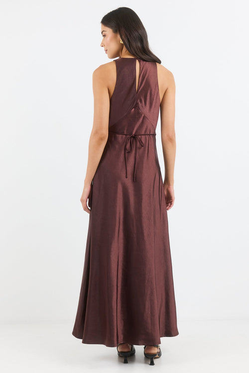 A woman wearing a sleeveless, floor-length dark plum maxi dress, shown from the back against a plain white studio background.