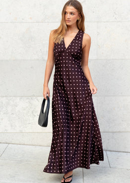 Woman wearing a dark sleeveless dress with white patterns against a light gray wall.