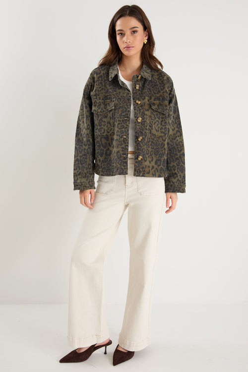 Woman wearing a patterned jacket and white pants on a plain background