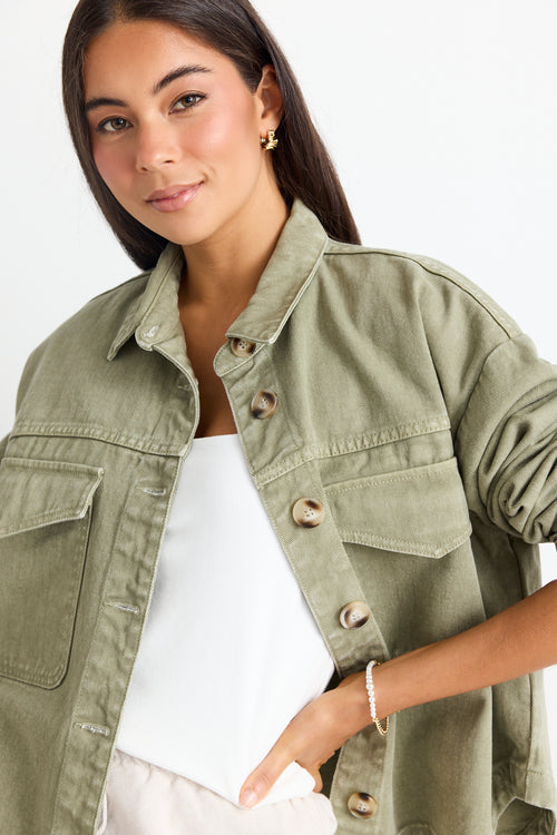 model wears a thick green cotton jacket over a white top and a beige linen skirt