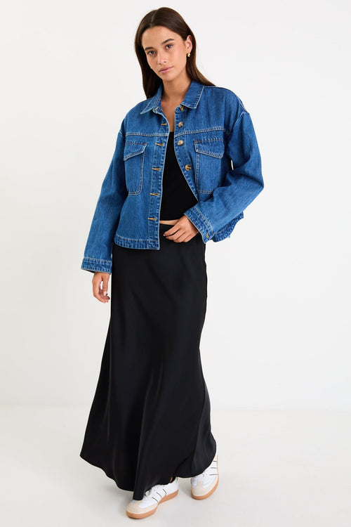 Woman wearing a blue denim jacket over a black outfit on a white background