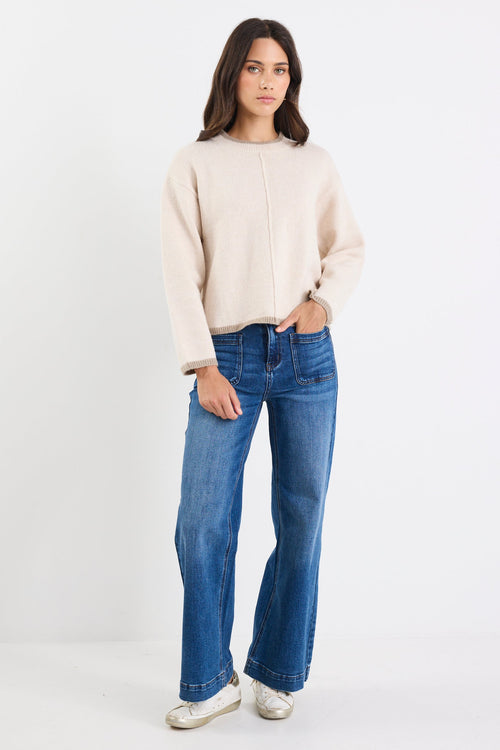 Woman wearing a beige sweater and blue jeans on a white background