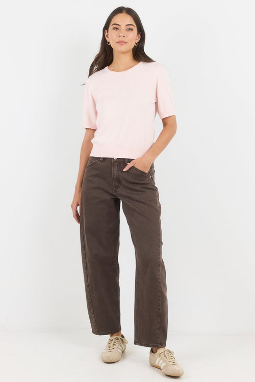 Woman wearing a light pink top and dark brown pants on a white background