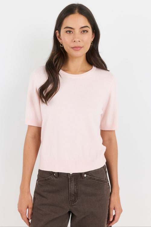 Woman wearing a light pink t-shirt and dark jeans on a white background