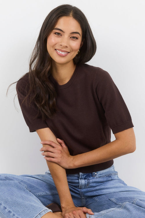 Woman sitting on the floor wearing a brown t-shirt and blue jeans against a white background