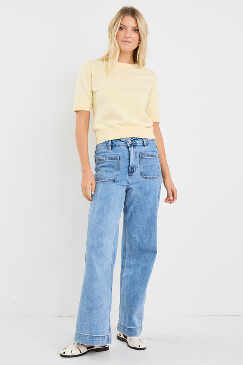 model wears a yellow knit tee with light blue jeans