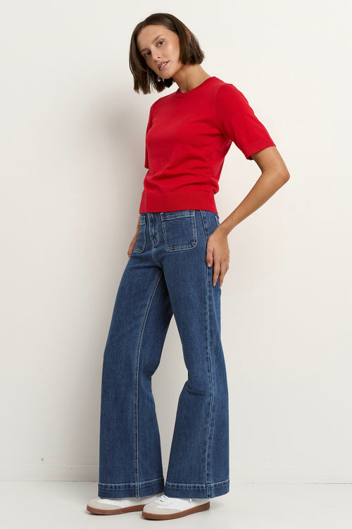 model wears a red knit t-shirt with dark blue wide leg jeans