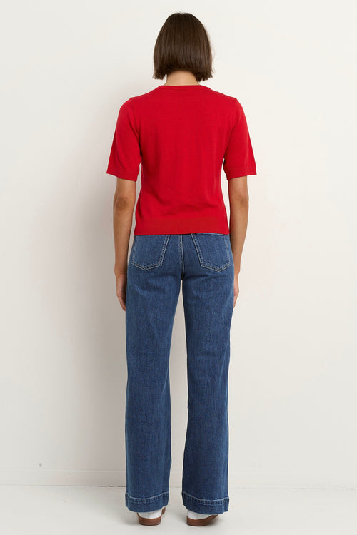 model wears a red knit t-shirt with dark blue wide leg jeans