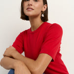 model wears a red knit t-shirt with dark blue wide leg jeans