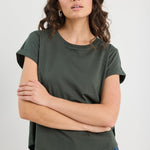 Woman wearing a green t-shirt and blue jeans against a plain background