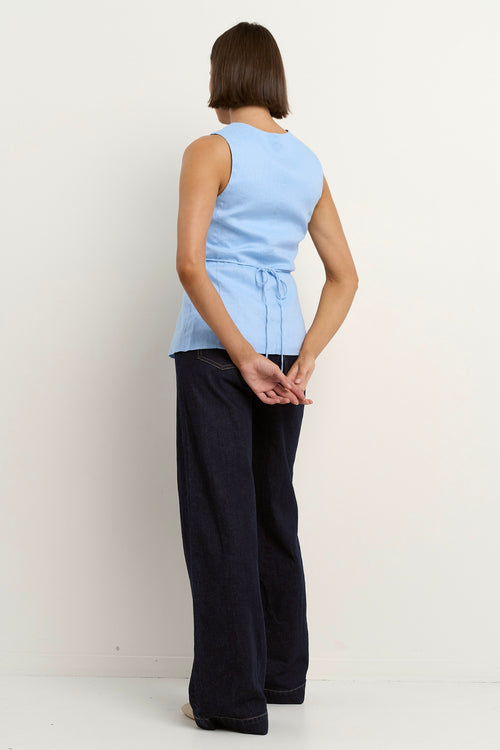 model wears a light blue linen vest with dark blue wide leg jeans