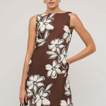 Brown sleeveless mini dress with a straight neckline and bold white floral print, styled with a loose A-line fit, worn by a model holding a woven handbag.