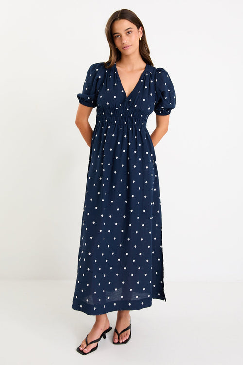 Model wearing a navy polka dot maxi dress with a V neckline, flutter sleeves and an elasticated waist