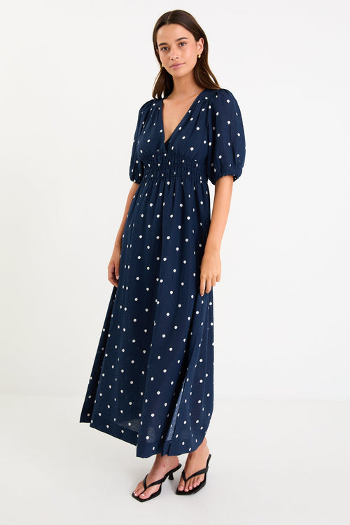 Model wearing a navy polka dot maxi dress with a V neckline, flutter sleeves and an elasticated waist